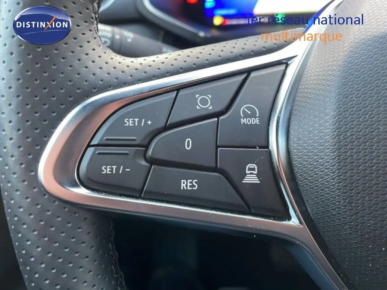 Gros plan sur les commandes noires du volant perforé d'une Renault Symbioz gris cassiopée métal, avec chrome autour.