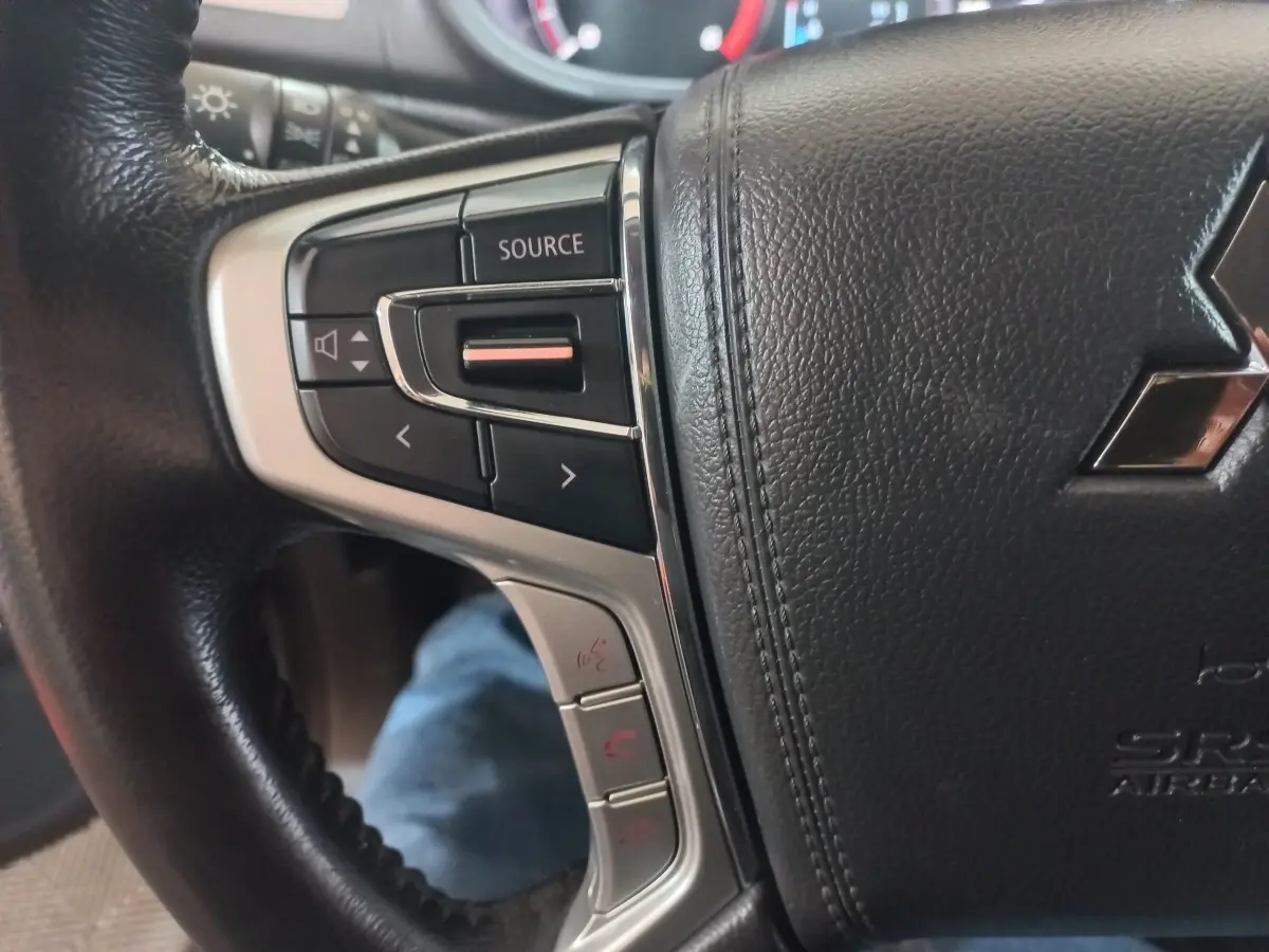 Gros plan sur le volant cuir noir du Mitsubishi L200 2020, avec commandes audio et téléphone intégrées à gauche.