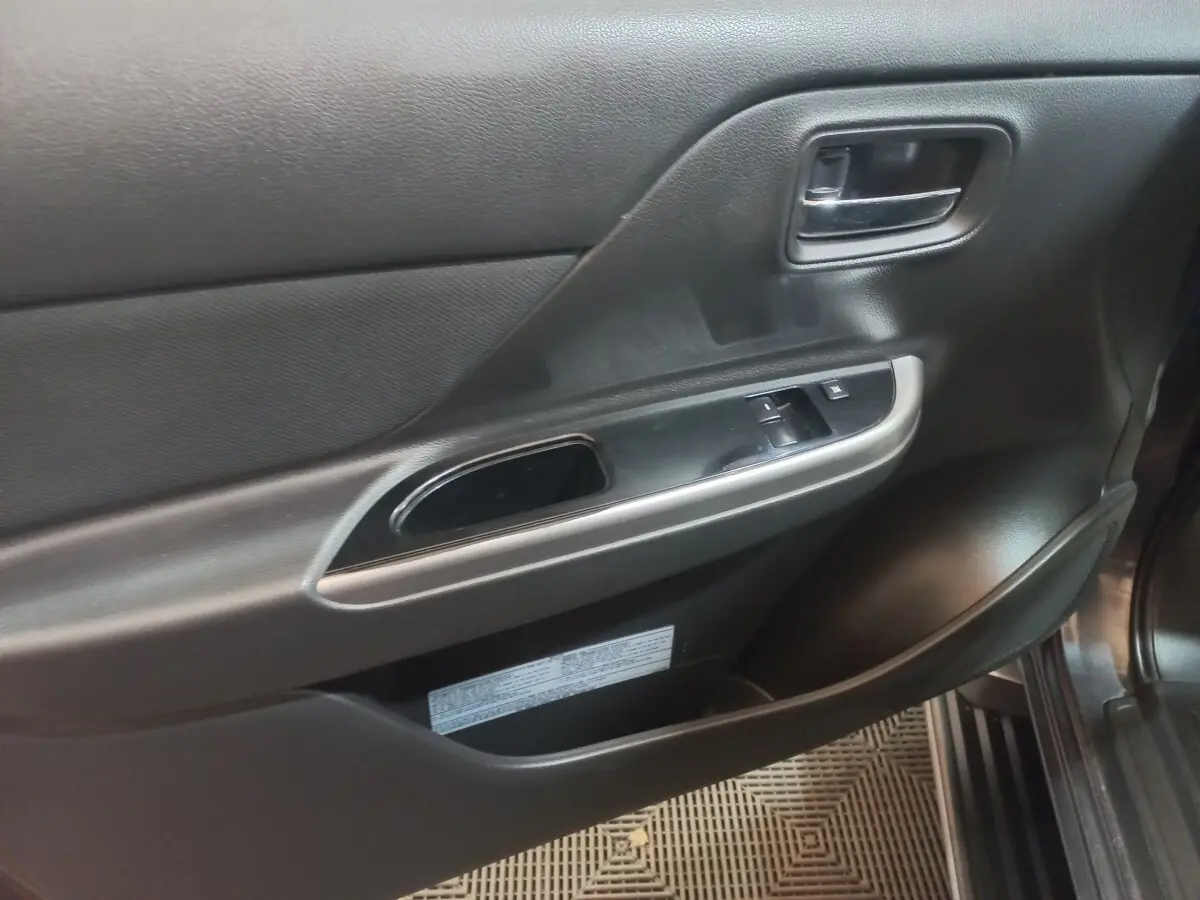Vue rapprochée de la porte intérieure côté conducteur du Mitsubishi L200 gris foncé, avec commandes de vitres et poignée chrome.
