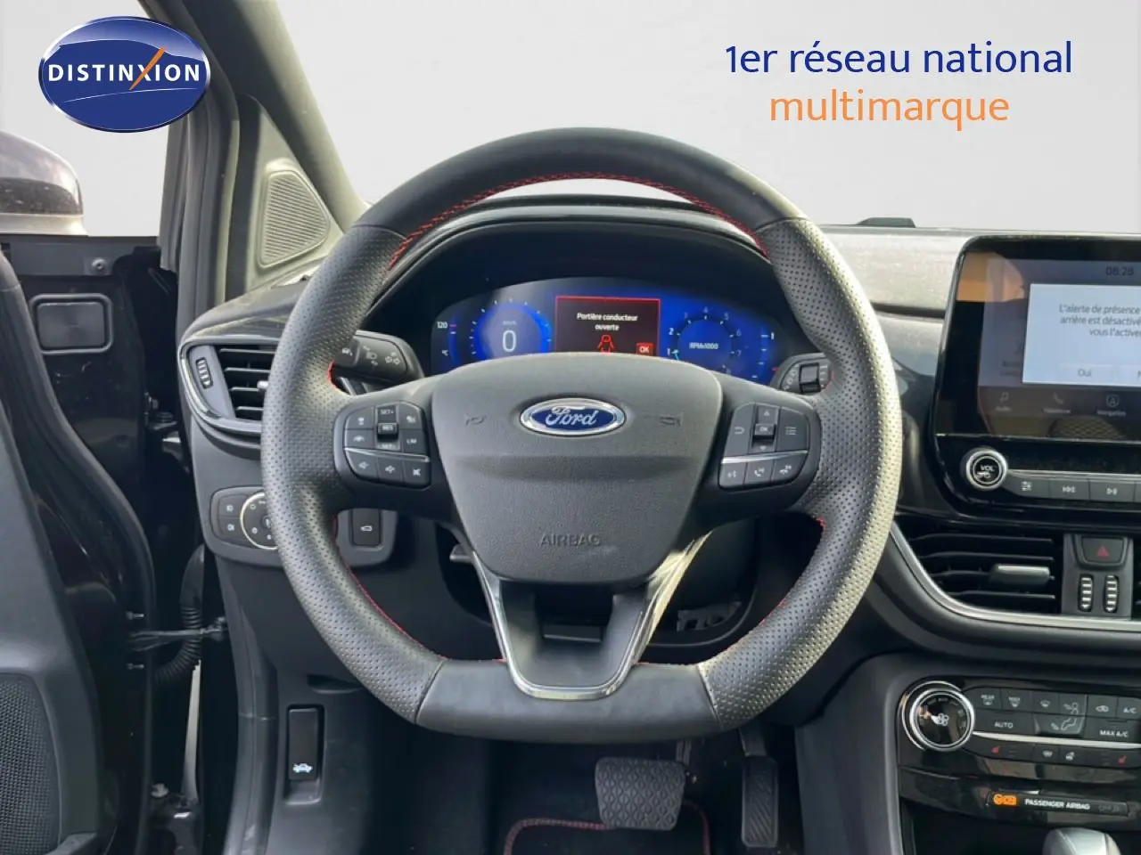Vue intérieure centrée sur le volant perforé noir avec surpiqûres rouges du Ford Puma 2023, tableau de bord et écran tactile visibles.