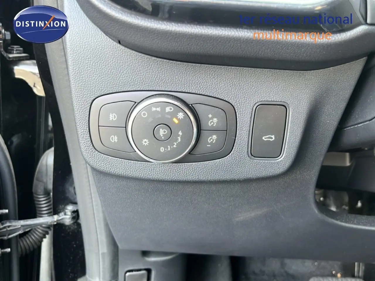 Détail du tableau de bord côté gauche avec commandes d’éclairage et bouton d’ouverture du coffre sur Ford Puma noir Agate Metal 2023.