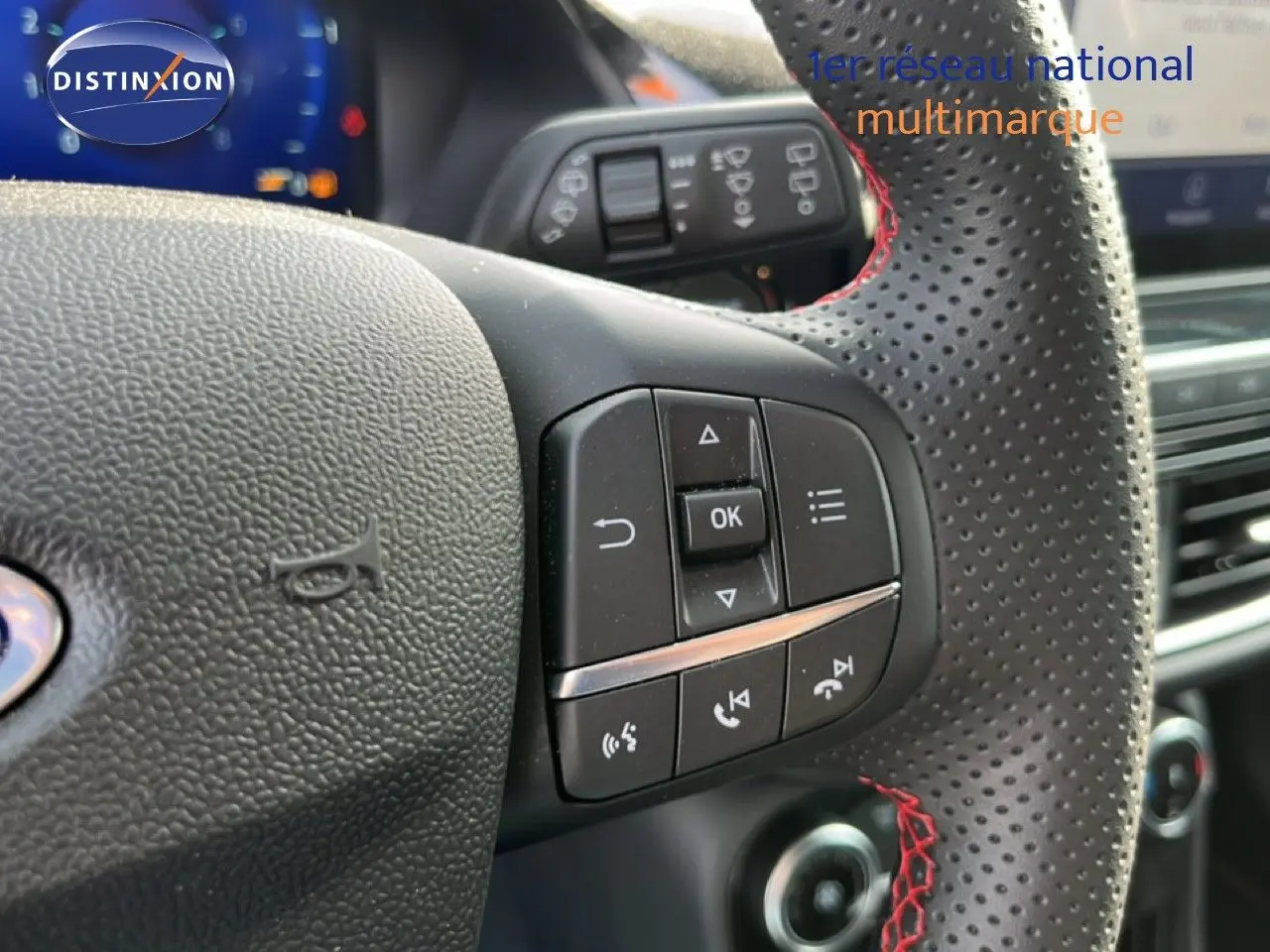 Gros plan sur le volant perforé avec surpiqûres rouges du Ford Puma noir agate, montrant les commandes multifonctions côté gauche.