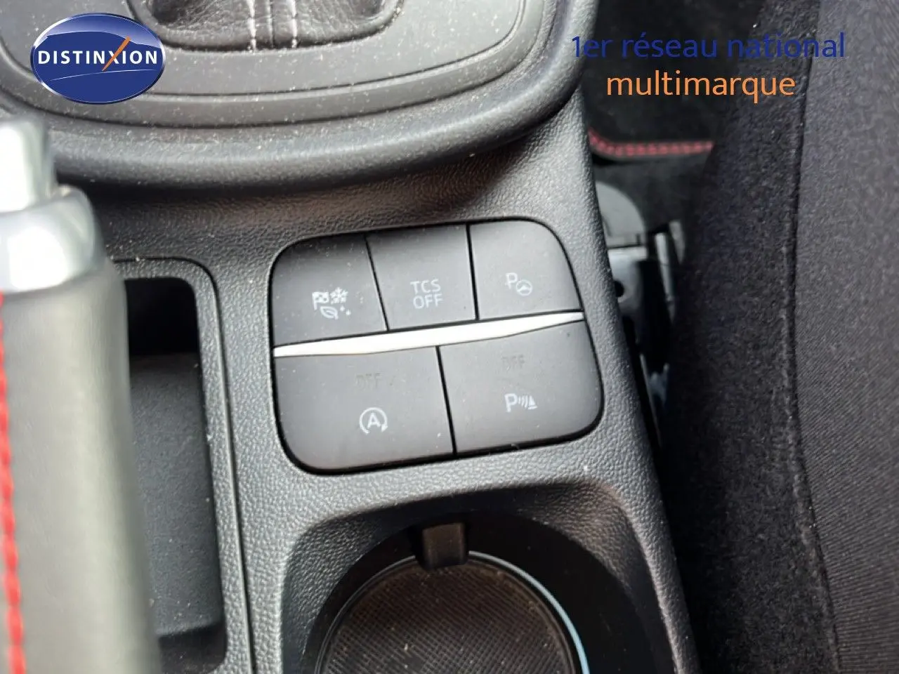Gros plan sur les commandes centrales et porte-gobelet du Ford Puma noir agate, avec surpiqûres rouges visibles sur le levier.