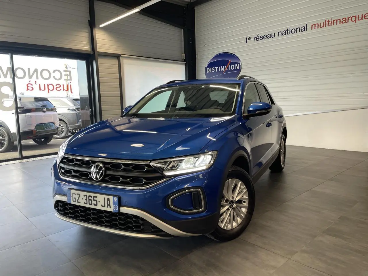 Volkswagen T-Roc bleu en 3/4 avant droit dans un showroom avec jantes alliage et calandre noire.
