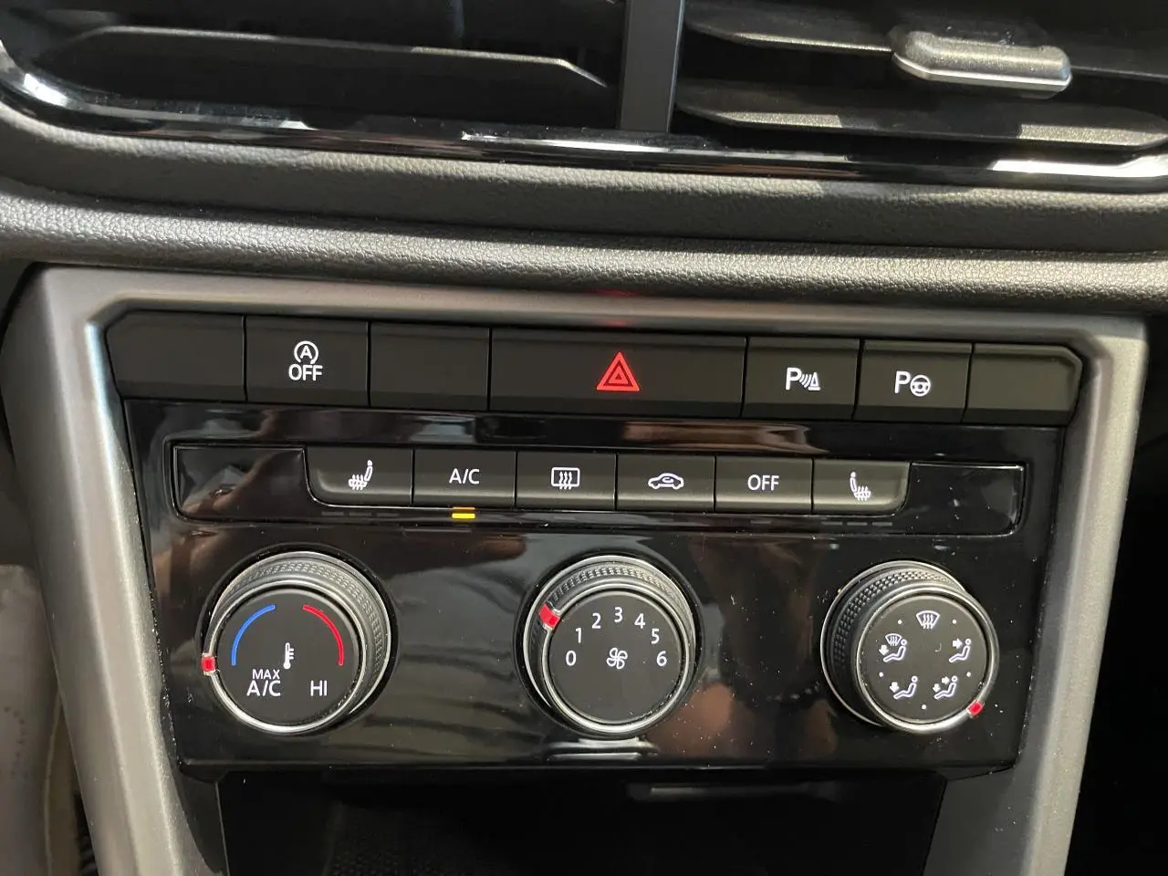 Gros plan sur la console centrale noire du Volkswagen T-Roc bleu, montrant les commandes de climatisation et d’alerte.