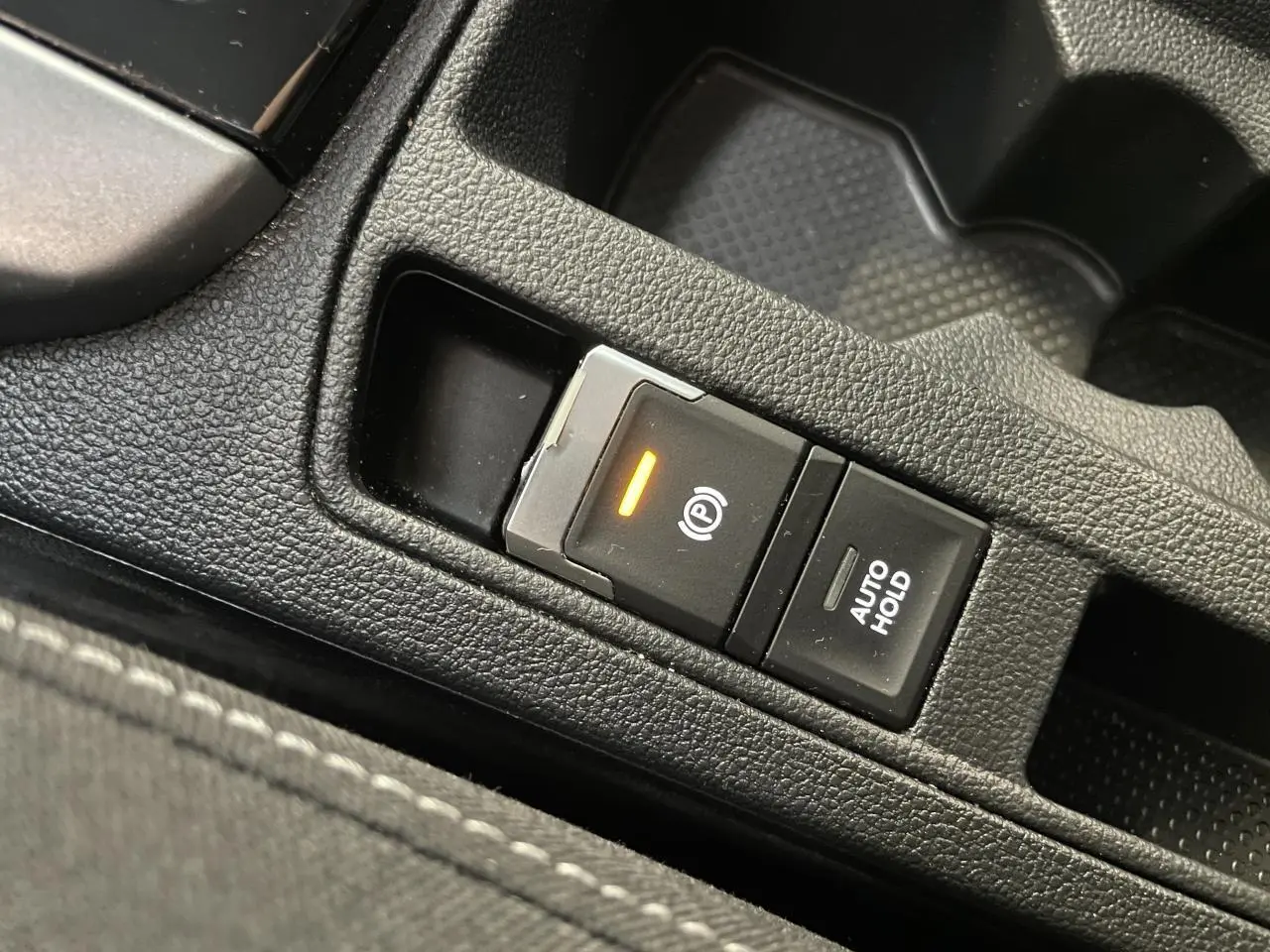 Gros plan sur le bouton de frein de stationnement électromécanique et fonction Auto Hold dans l'habitacle noir du Volkswagen T-Roc.
