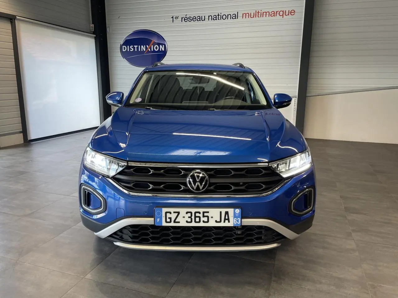 Vue avant d'un Volkswagen T-Roc bleu 2022 avec calandre noire et détails argentés en showroom.