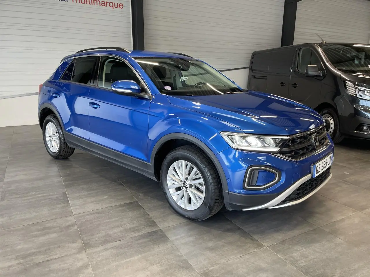 Volkswagen T-Roc bleu en 3/4 avant droit, avec jantes alliage et détails noirs sur les bas de caisse.