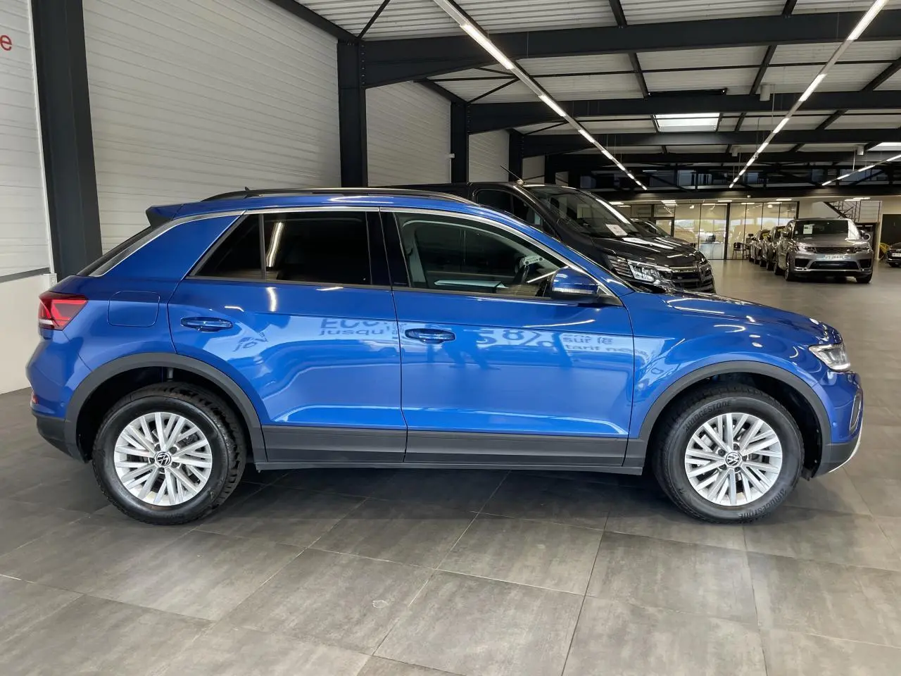 Vue latérale droite d'un Volkswagen T-Roc bleu 2022 en showroom avec jantes alliage et vitres teintées.