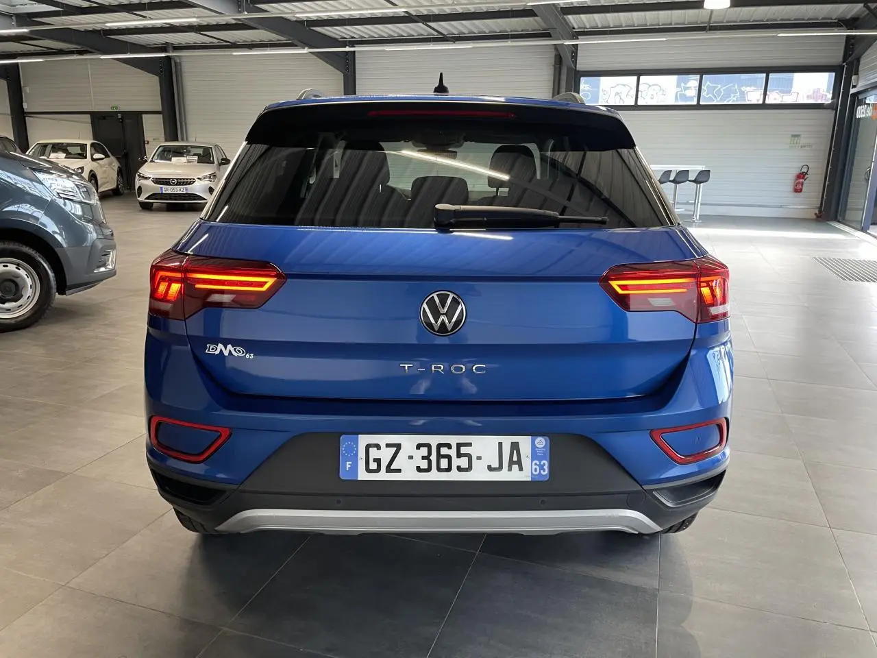 Vue arrière d'un Volkswagen T-Roc bleu 2022 avec feux LED allumés dans un showroom.