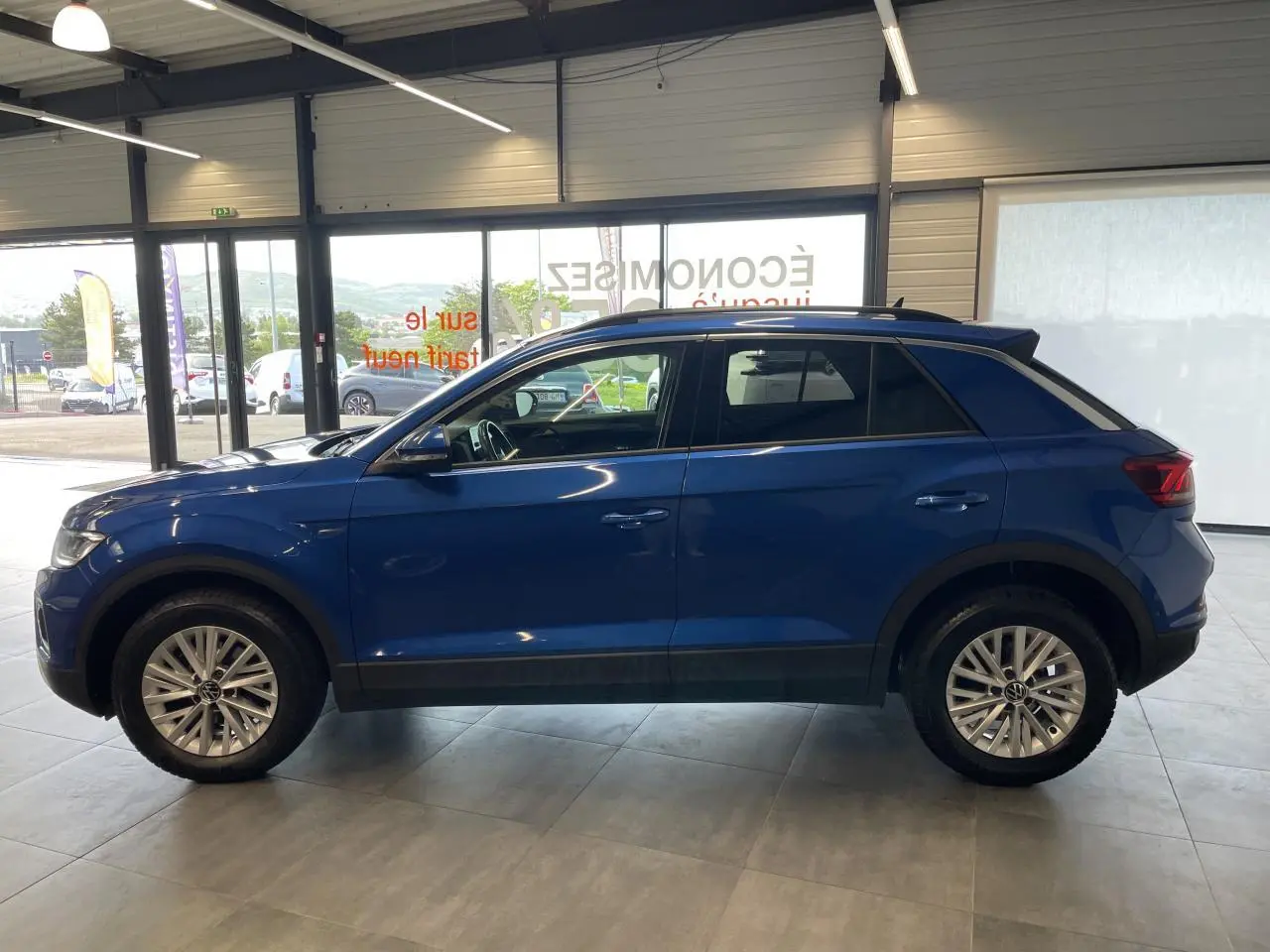 Volkswagen T-Roc bleu en vue de profil côté gauche, avec jantes alliage et vitres teintées en showroom.