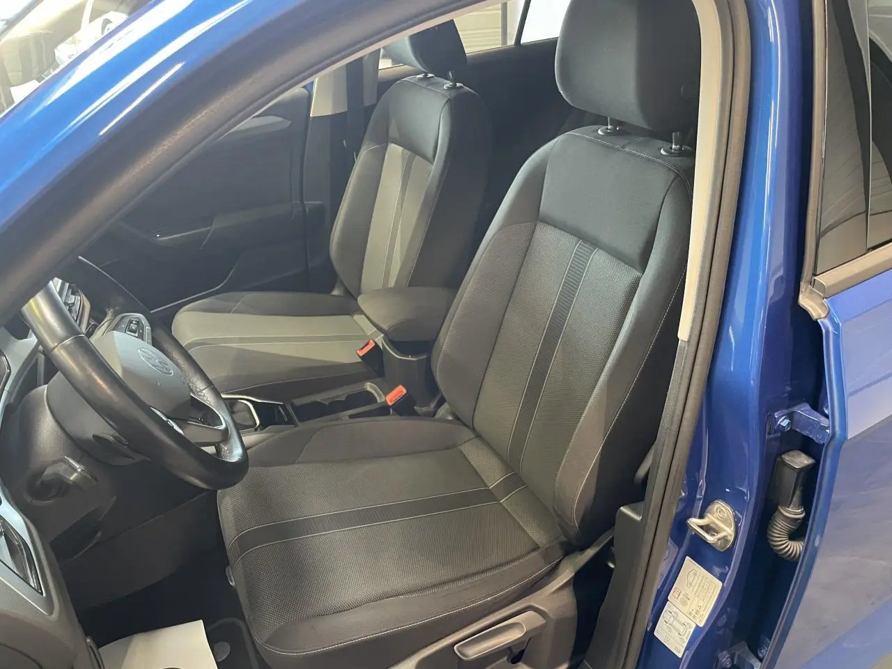 Vue intérieure côté conducteur du Volkswagen T-Roc bleu 2022, sièges tissu noir avec accoudoir central.