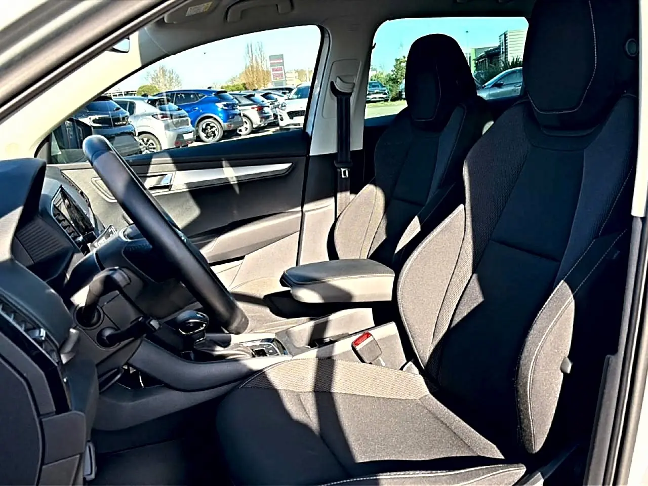 Vue intérieure côté conducteur du Skoda Karoq gris 2025, mettant en valeur les sièges avant et l'accoudoir central.