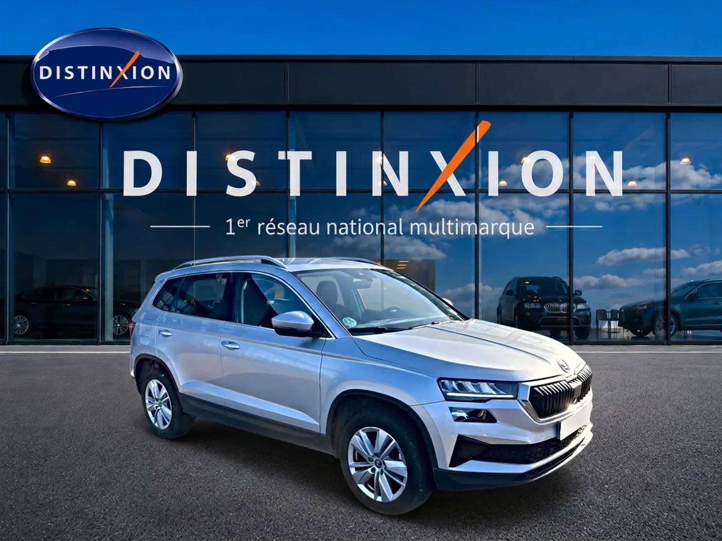 SKODA KAROQ gris 3/4 avant droit, SUV compact avec jantes alu et barres de toit devant vitrine Distinxion.