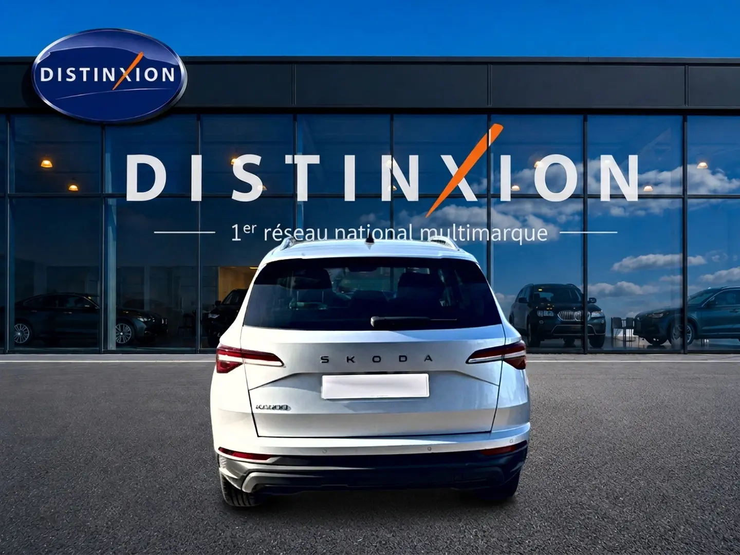 Vue arrière d'un Skoda Karoq gris 2025 garé devant une vitrine avec logo Distinxion en arrière-plan.