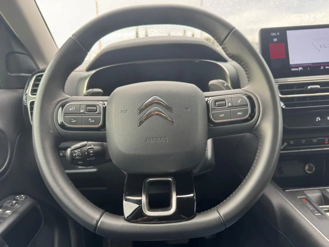 Vue rapprochée du volant multifonction noir du Citroën C5 Aircross 2024 avec commandes intégrées et tableau de bord partiel.
