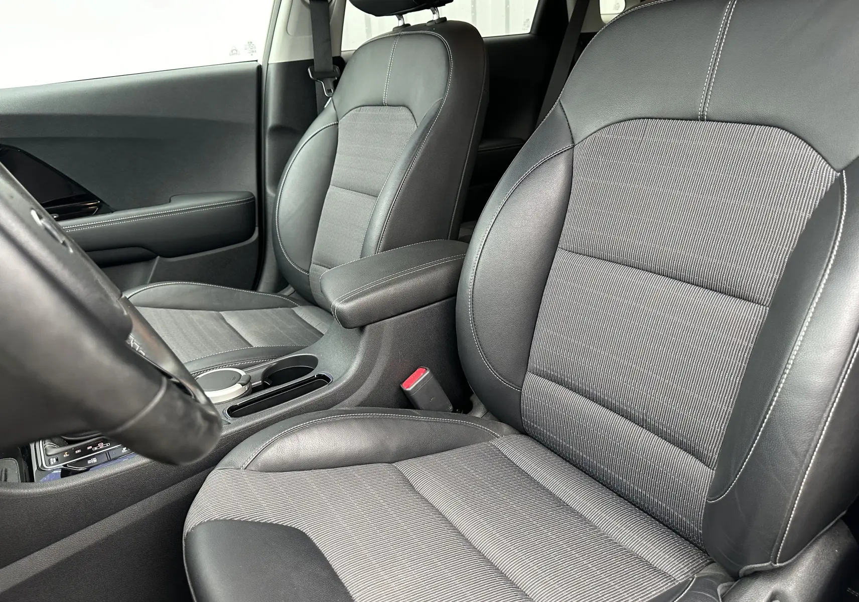 Vue rapprochée des sièges avant en cuir et tissu gris du Kia Niro hybride rechargeable, avec accoudoir central et console visible.