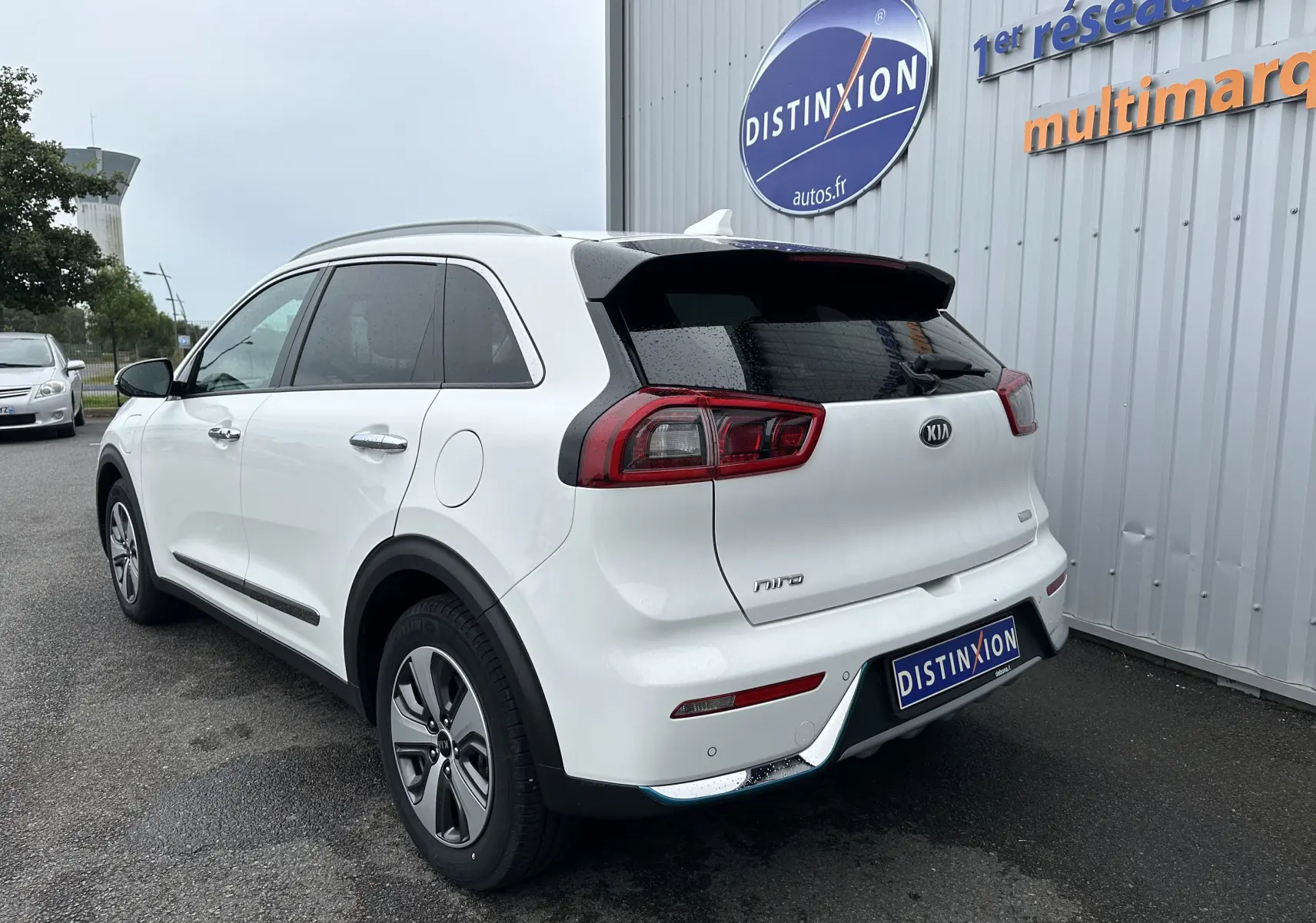 Vue 3/4 arrière droite d'un KIA Niro blanc céleste hybride rechargeable, avec feux arrière LED et jantes spécifiques.