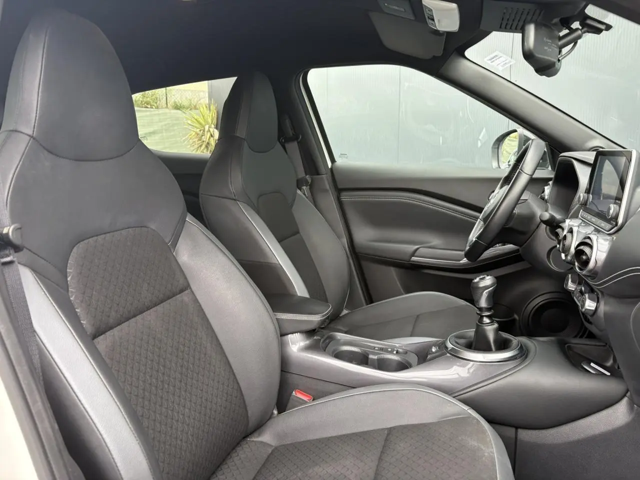 Intérieur noir et gris du Nissan Juke 2023, vue côté gauche montrant sièges, volant et levier de vitesse manuel.