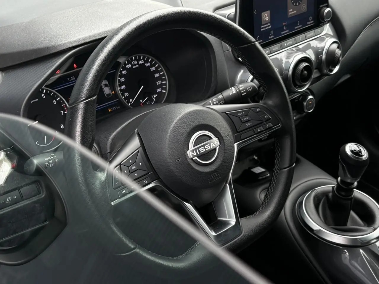 Vue rapprochée de l'intérieur du Nissan Juke blanc perle 2023, volant multifonction et levier de vitesse manuel visibles.