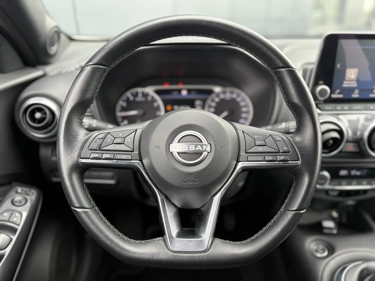 Volant en cuir noir de Nissan Juke 2023 avec commandes intégrées, tableau de bord et écran tactile en arrière-plan.