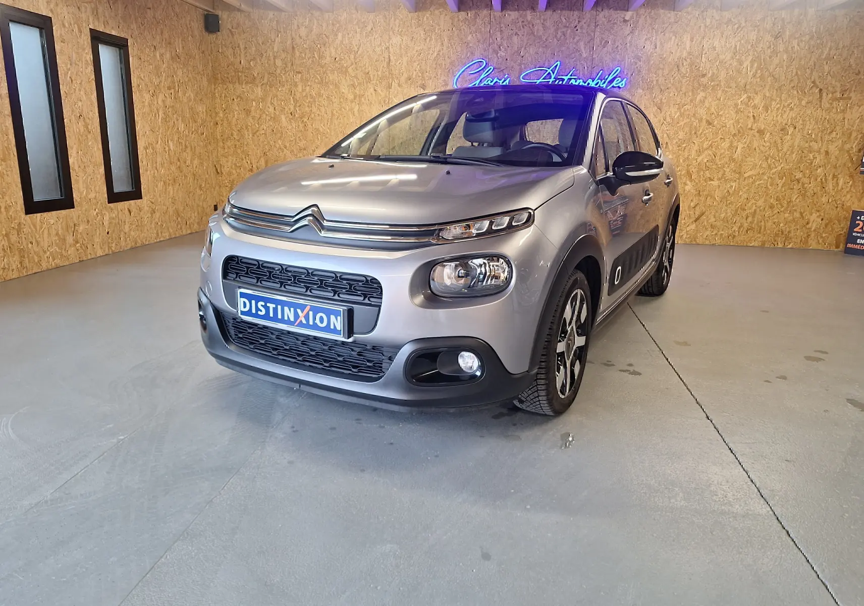 Citroën C3 gris en 3/4 avant droit, avec jantes aluminium et détails noirs sur les rétroviseurs et bas de caisse.