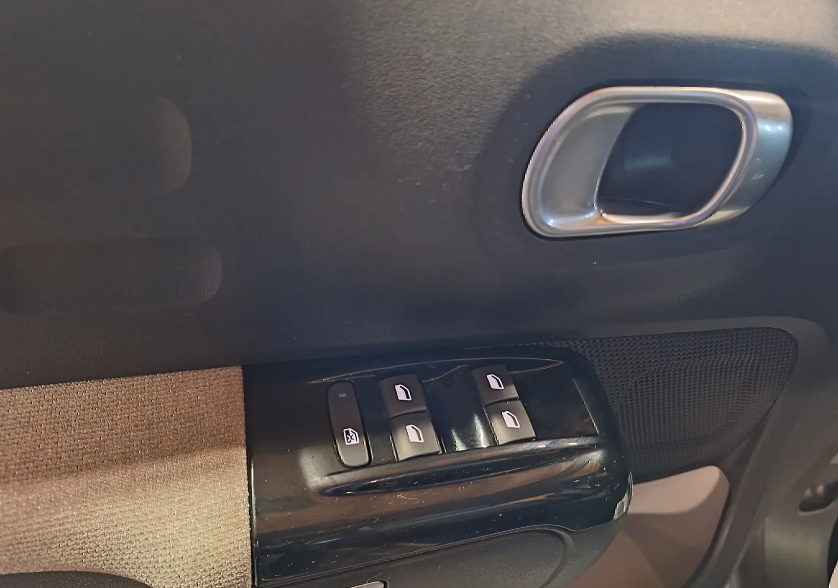 Gros plan sur la commande des vitres électriques côté gauche, avec poignée intérieure argentée et tissu gris Mica.