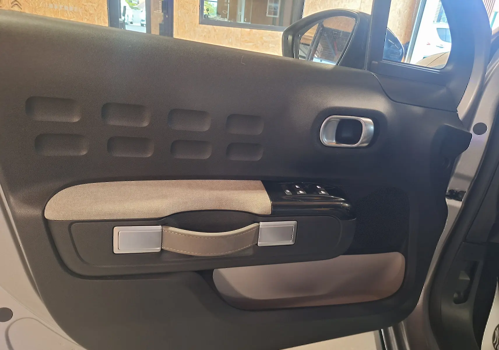 Vue intérieure côté gauche de la porte avant grise de la Citroën C3 avec poignée en tissu beige et commandes de vitres.