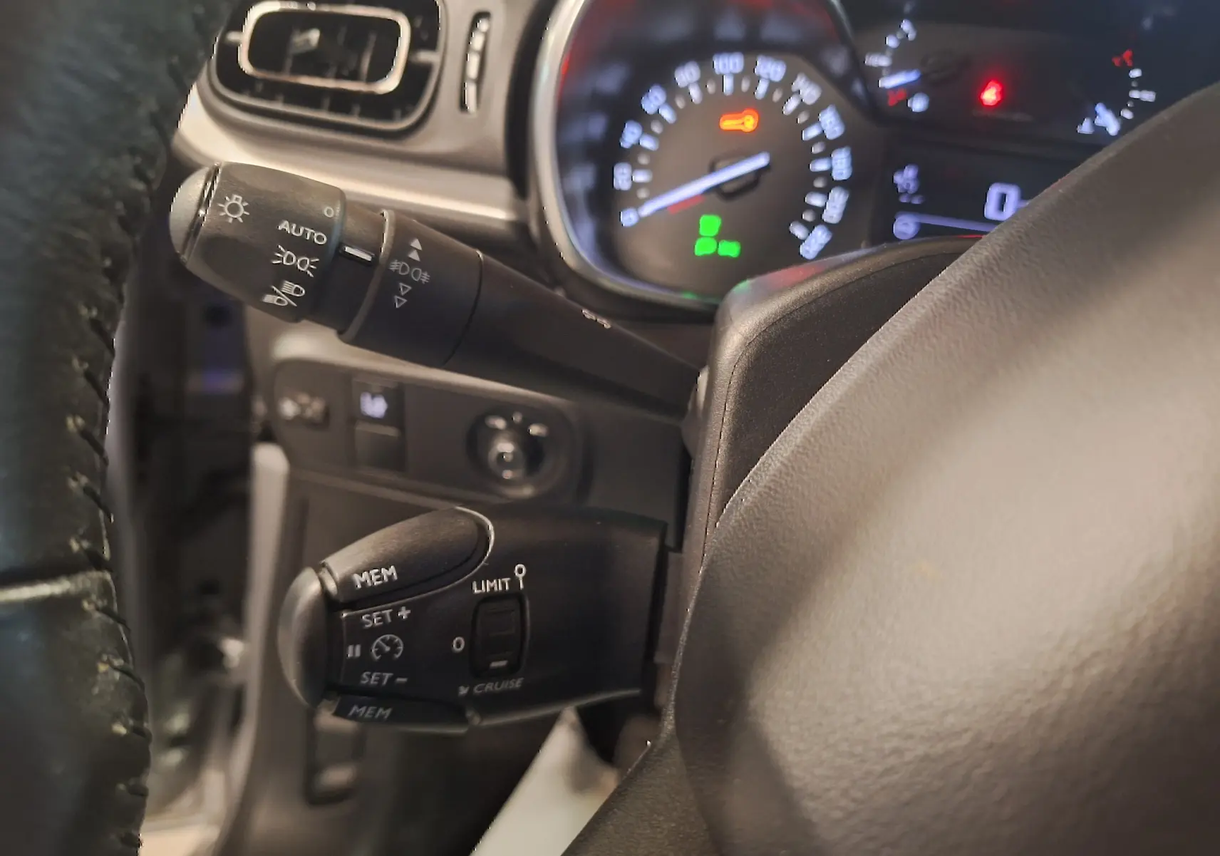 Gros plan sur le volant cuir et les commandes de régulateur de vitesse de la Citroën C3 gris, tableau de bord éclairé.
