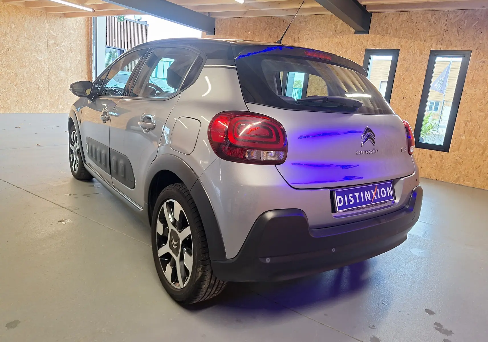Vue 3/4 arrière droite d'une Citroën C3 gris avec toit noir et jantes alliage dans un garage lumineux.