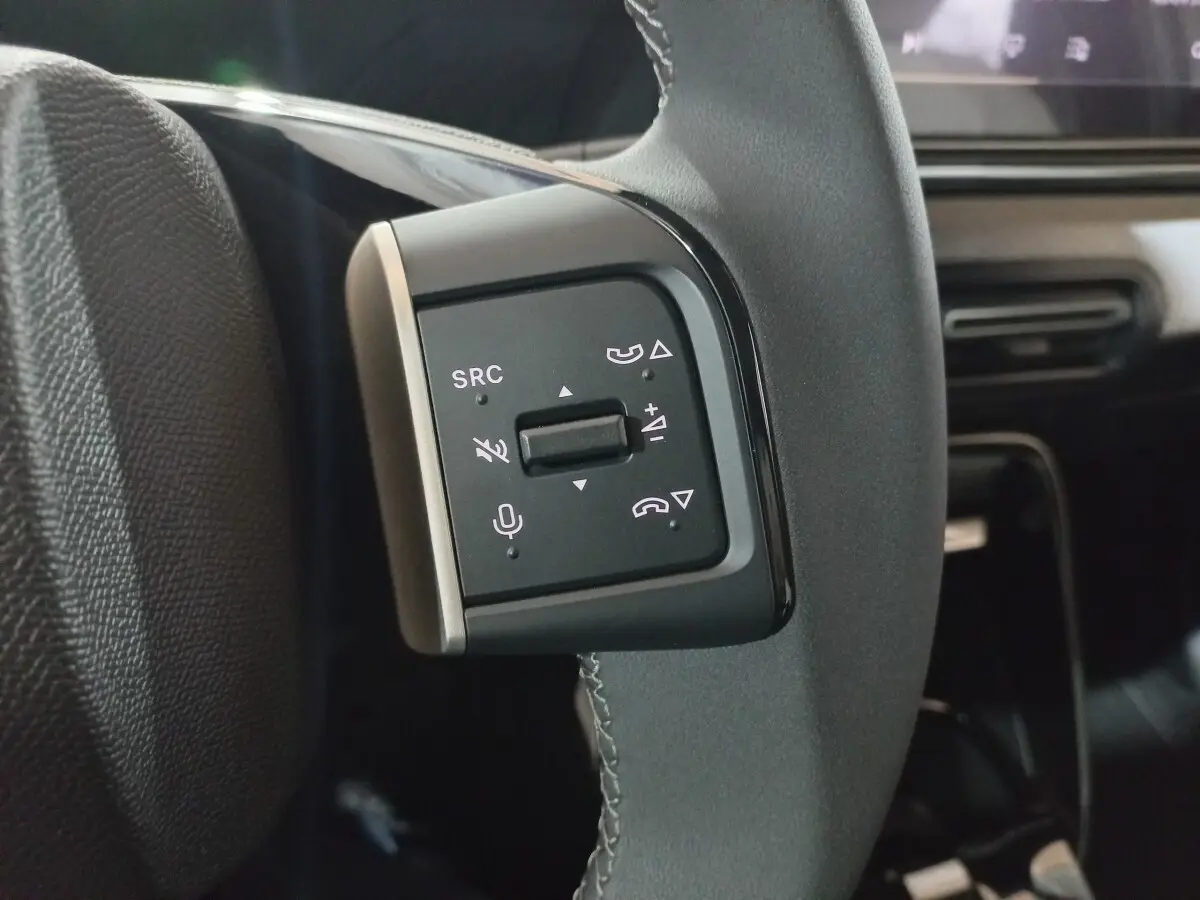 Gros plan sur les commandes gauche du volant cuir gris du Citroën C3 hybride 2025, avec boutons multifonctions visibles.