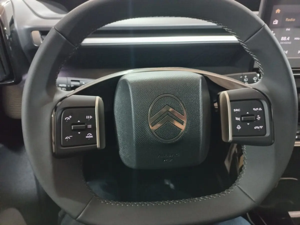 Vue rapprochée du volant cuir noir de la Citroën C3 hybride 2025 avec commandes multifonctions intégrées.