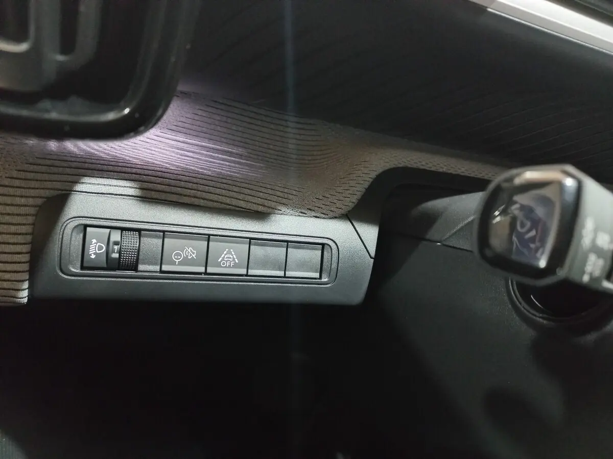 Gros plan sur les commandes de réglage des phares et aides à la conduite dans une Citroën C3 hybride gris foncé, côté conducteur.