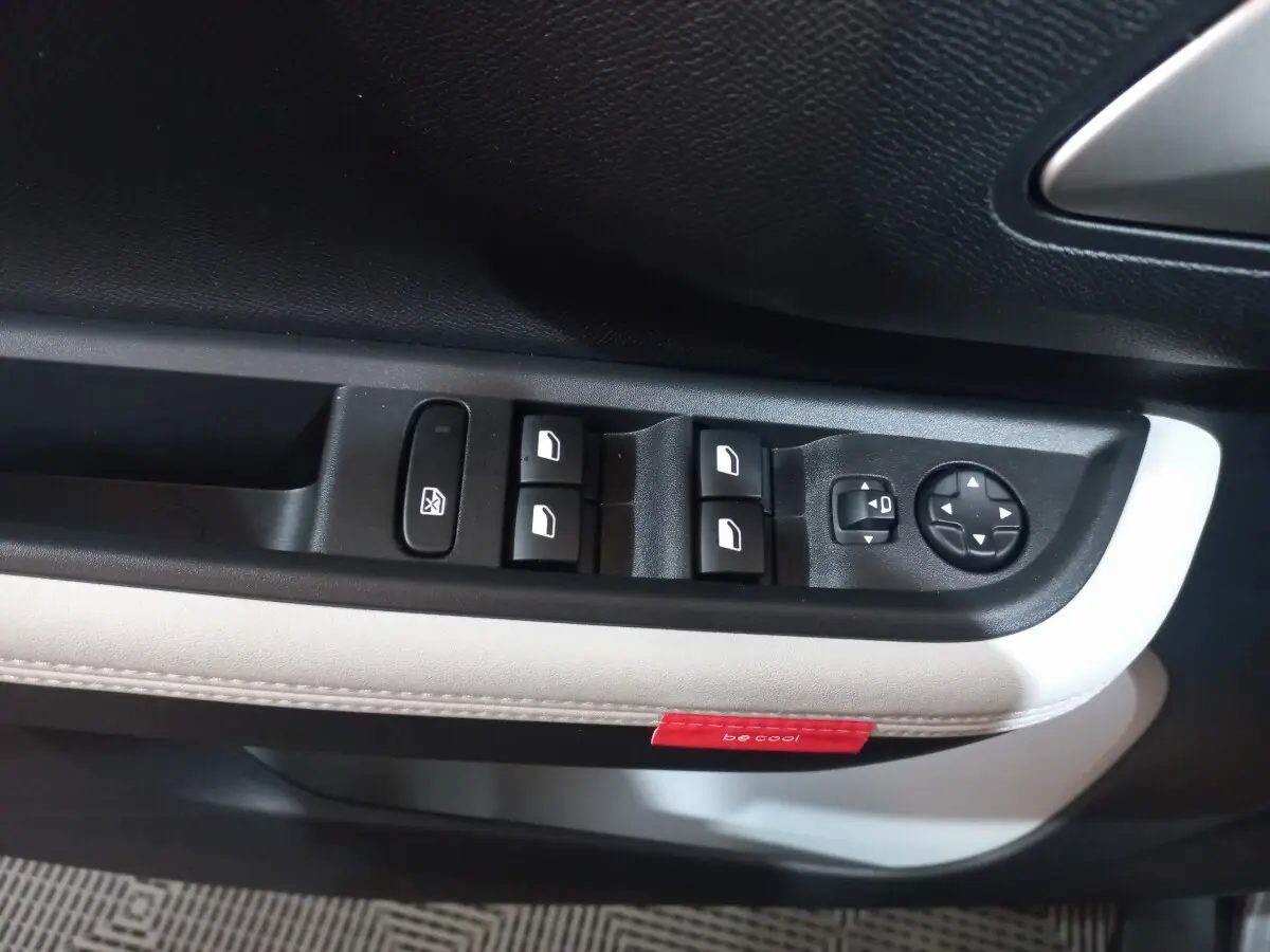 Gros plan sur la commande des vitres et rétroviseurs côté conducteur, garniture noire et blanche avec étiquette rouge "be cool"
