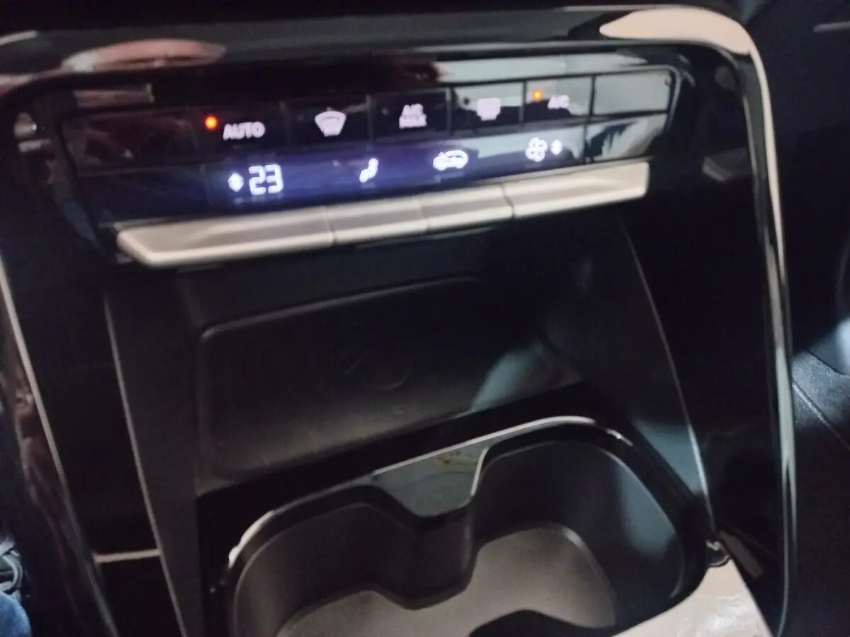 Vue rapprochée de la console centrale noire de la Citroën C3 hybride 2025 avec commandes climatisation et zone de recharge par induction.