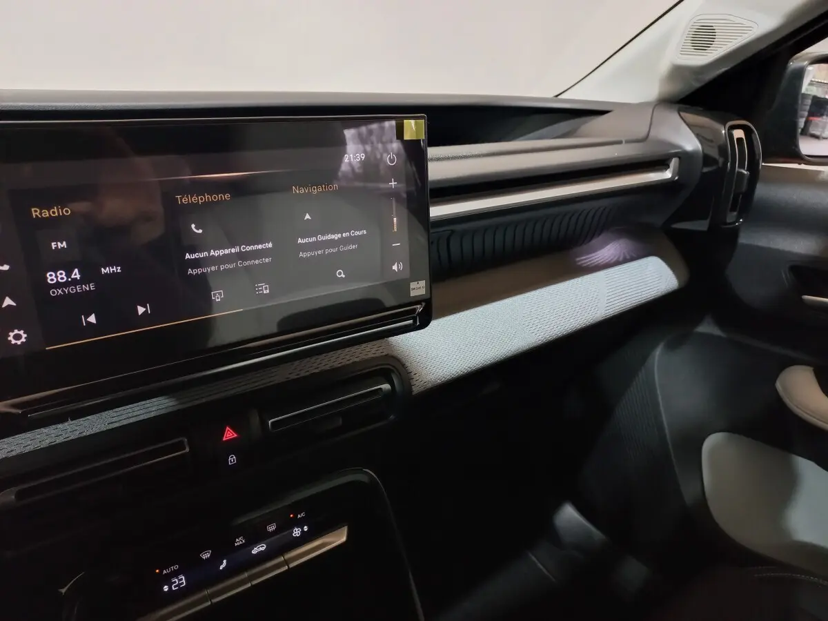 Vue intérieure côté passager du tableau de bord de la Citroën C3 hybride 2025 avec écran tactile et garniture gris clair.