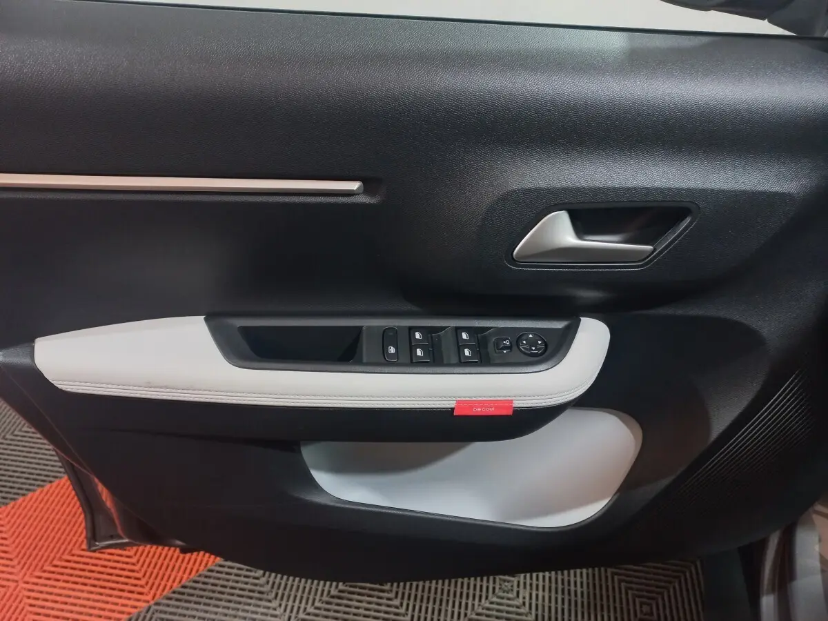 Vue rapprochée de la porte avant gauche de la Citroën C3 hybride 2025, avec garniture noire et blanche et commandes électriques.