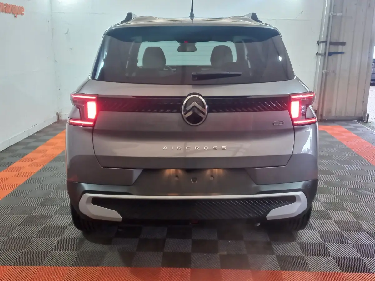 Vue arrière d'une Citroën C3 gris foncé avec feux allumés dans un garage au sol damier noir et orange.