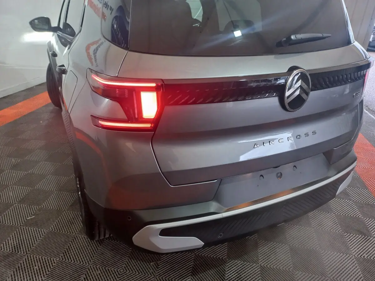 Vue 3/4 arrière gauche d'un Citroën Aircross gris foncé avec feux arrière allumés et logo central chromé.