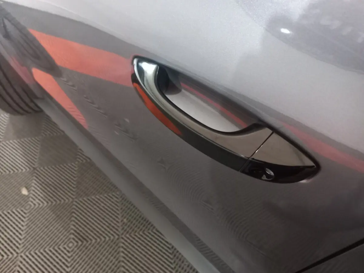 Poignée de porte côté droit d'une Citroën C3 hybride gris foncé avec reflet rouge sur la carrosserie.