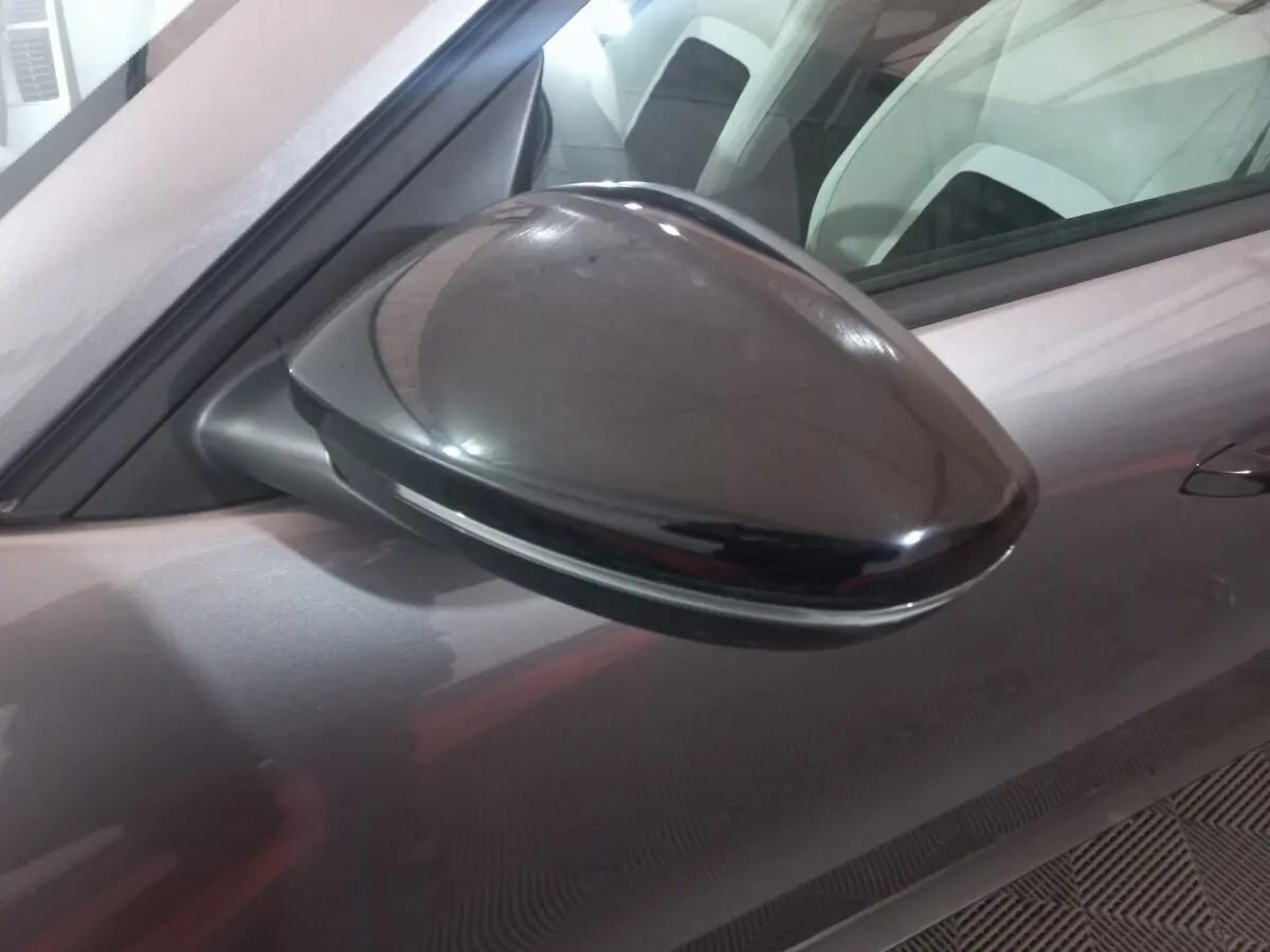 Rétroviseur côté conducteur noir brillant sur Citroën C3 hybride gris foncé, vue rapprochée en intérieur.