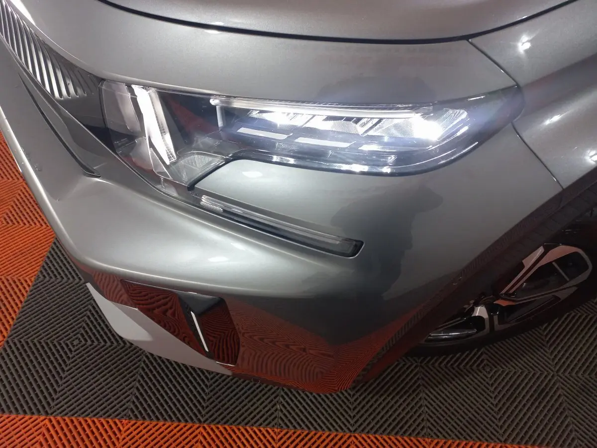 Gros plan sur le phare avant droit d'une Citroën C3 hybride 2025 gris foncé avec détail du pare-chocs et jante.