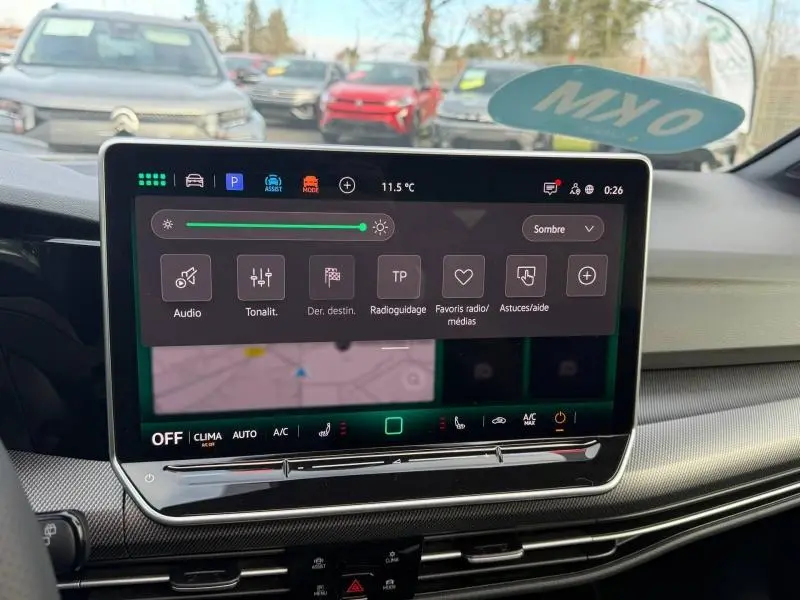Vue intérieure centrée sur l'écran tactile du tableau de bord de la Volkswagen Golf gris 2025, avec commandes numériques visibles.