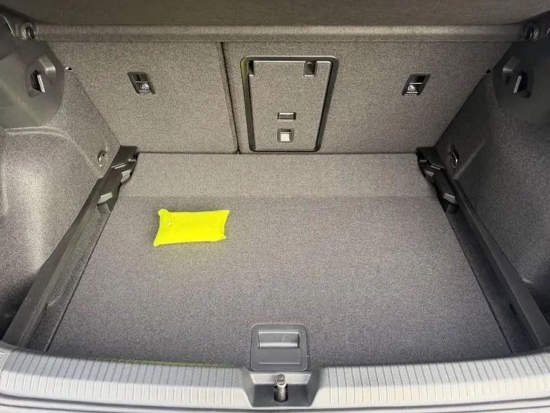 Coffre ouvert de la Volkswagen Golf 1.5 eTSI R-Line gris 2025, vue plongeante sur l’espace de chargement avec un coussin jaune.
