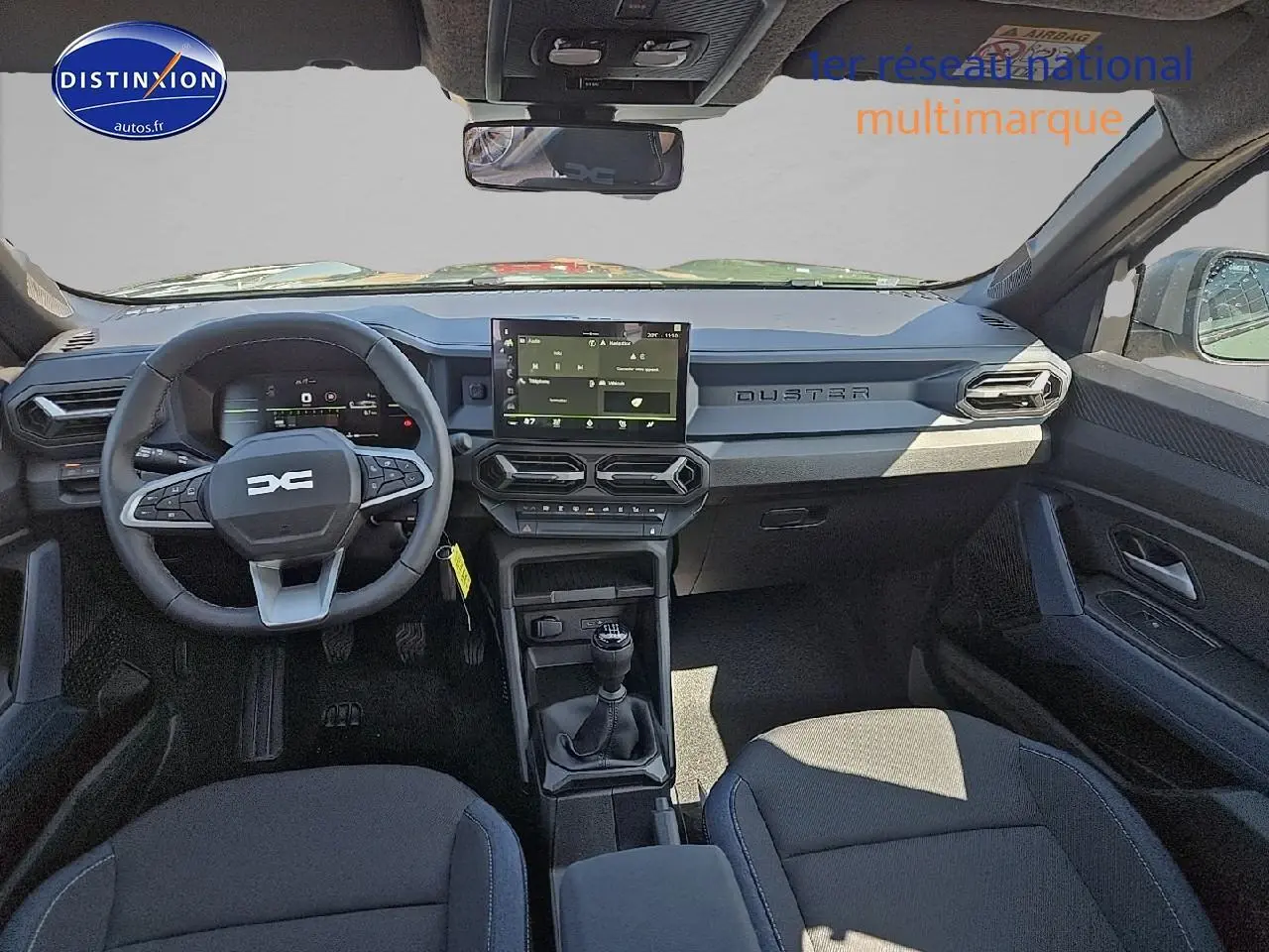 Vue intérieure avant du Dacia Duster 2025 avec tableau de bord moderne, écran tactile et volant multifonction noir.
