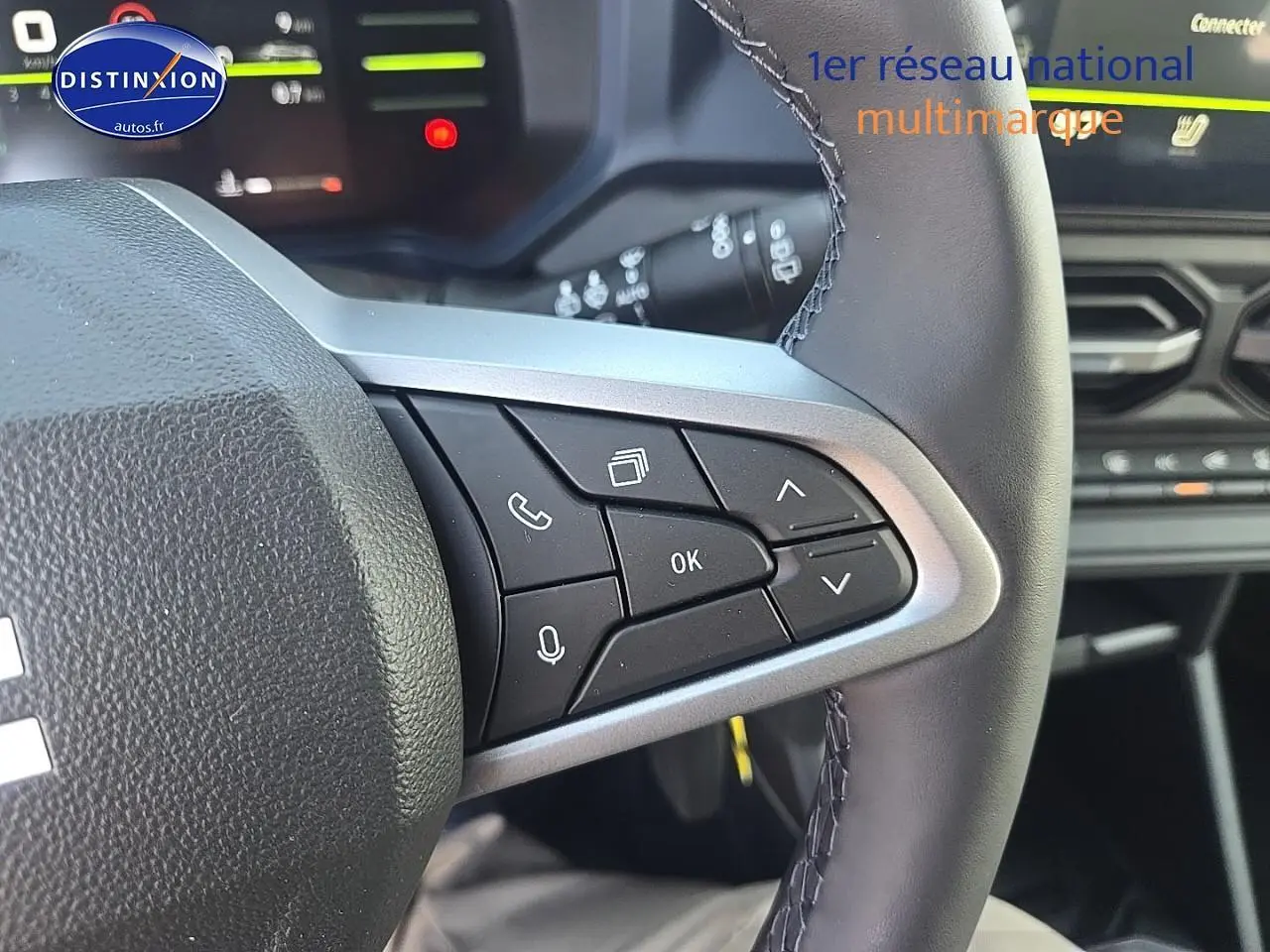 Gros plan sur les commandes au volant multifonction du Dacia Duster 2025, intérieur noir avec écran tactile en arrière-plan.