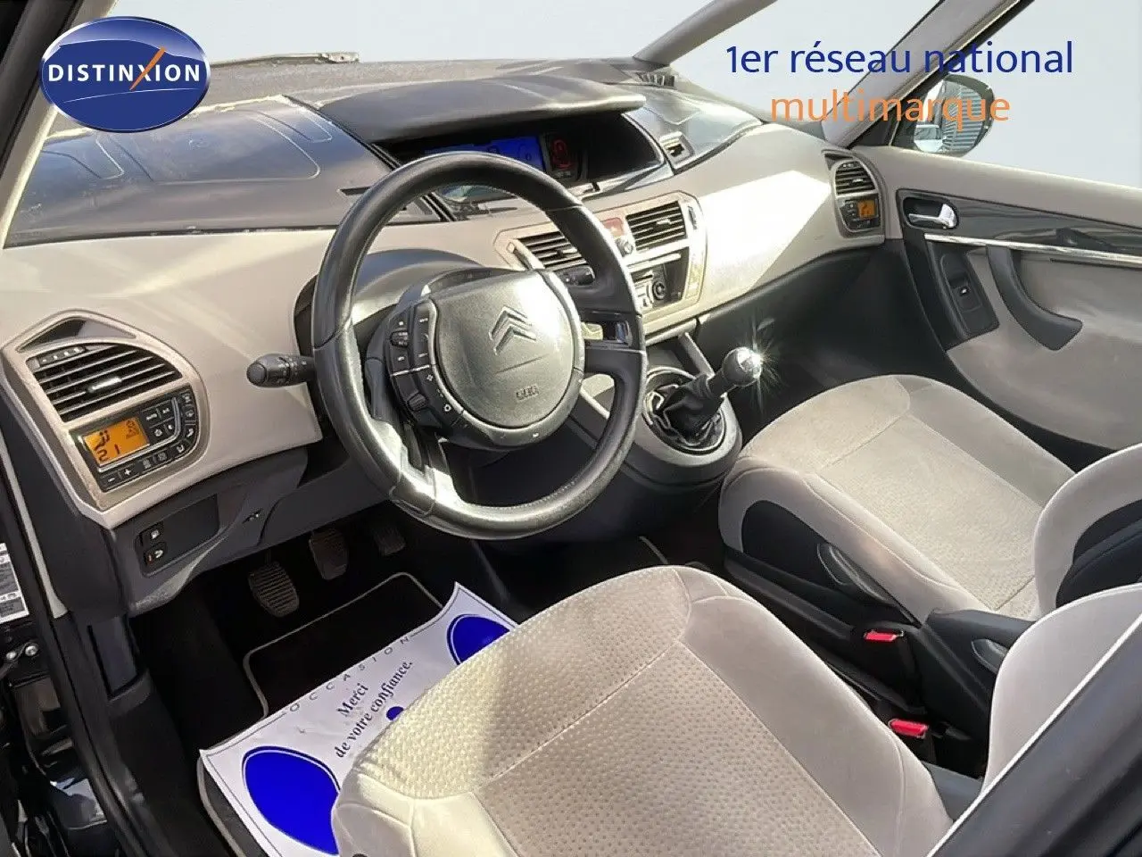 Vue intérieure côté conducteur de la Citroën C4 Picasso 2008, volant cuir noir et sièges tissu beige clair.