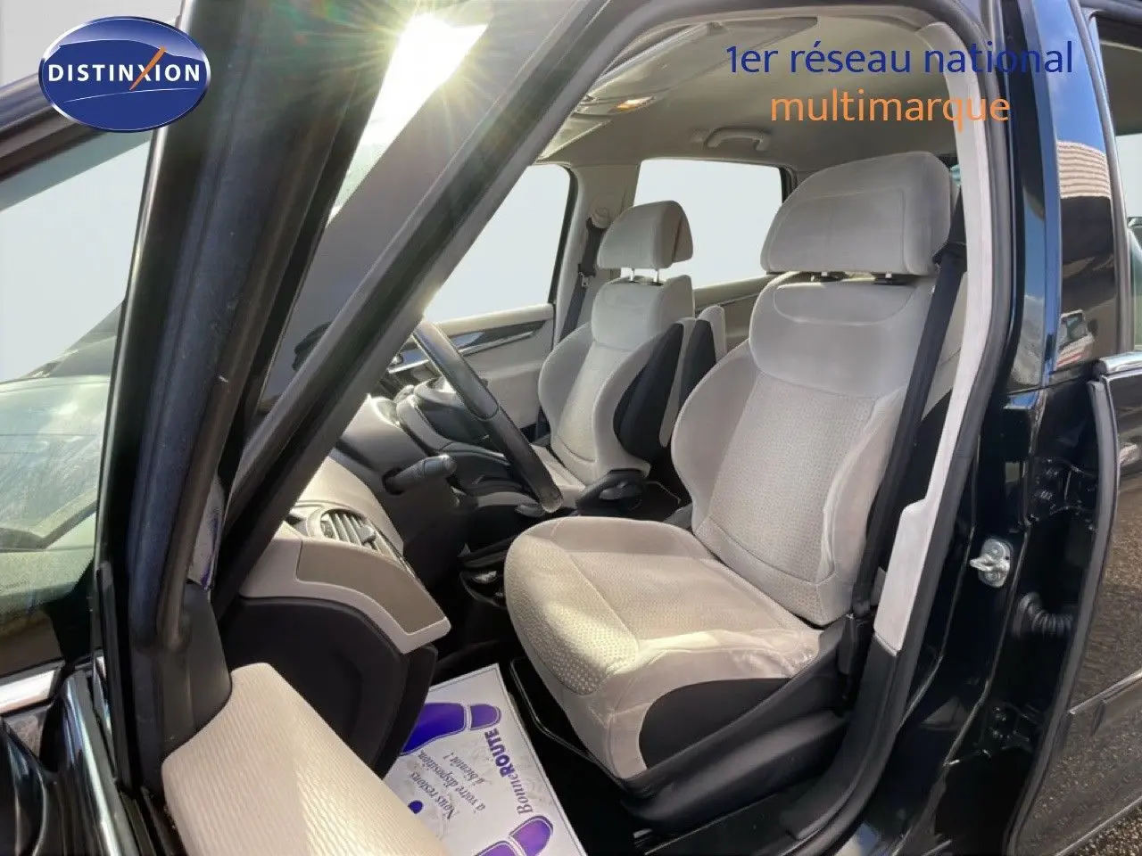 Vue intérieure côté conducteur d'une Citroën C4 Picasso noire métal de 2008, sièges tissu beige clair et volant cuir.