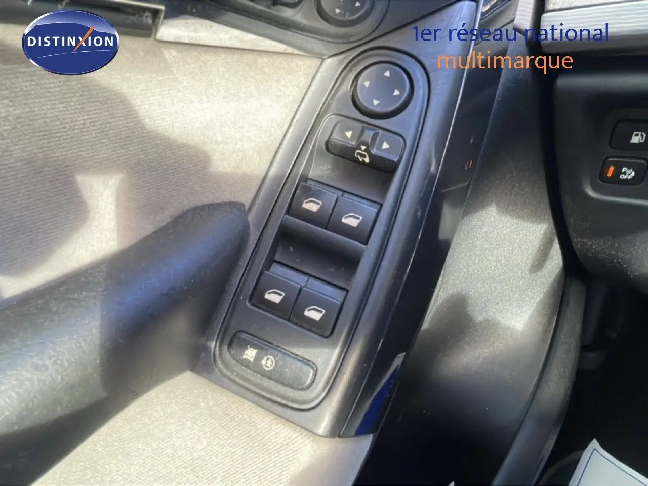 Vue rapprochée des commandes des vitres électriques et rétroviseurs côté conducteur d'une Citroën C4 Picasso noir métal de 2008.