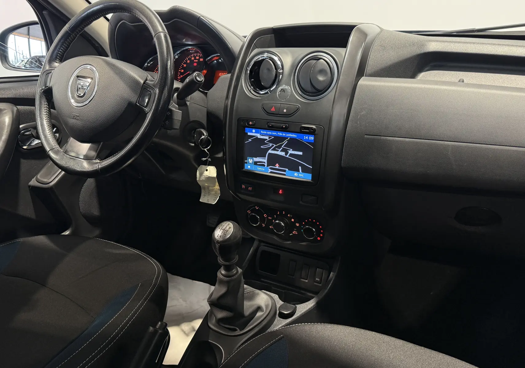 Vue intérieure côté conducteur du Dacia Duster 2015 bleu, montrant le volant, la boîte manuelle et l'écran de navigation.